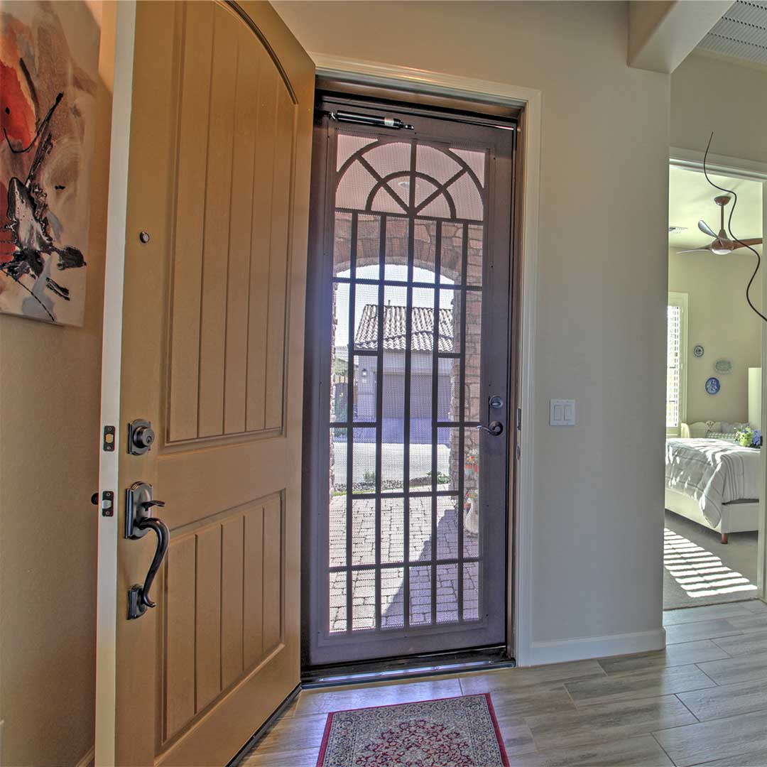 View of a front door, from the inside of a house, looking out the iron screen door that allows airflow in the home