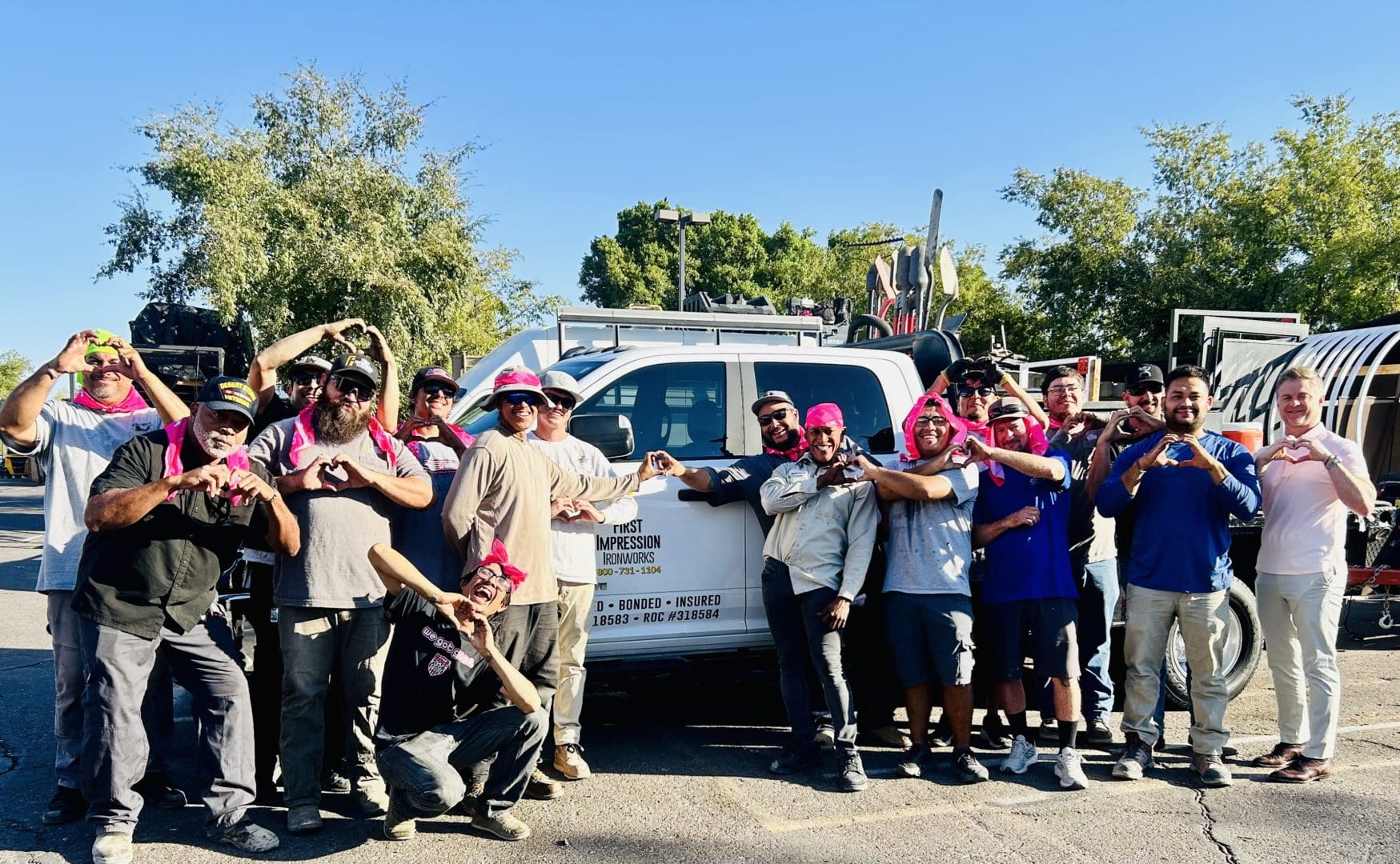 Large group of First Impression Ironworks employees wearing pink, standing in front of a First Impression Ironworks truck