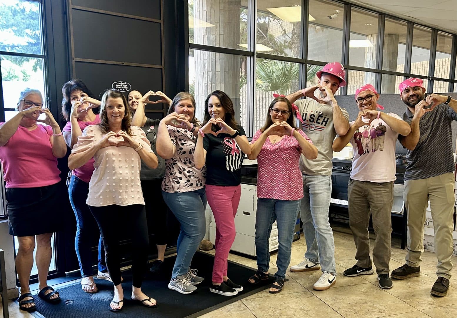 Group of First Impression Ironworks Employees wearing pink and holding up heart hands in support of Breast Cancer Awareness Month