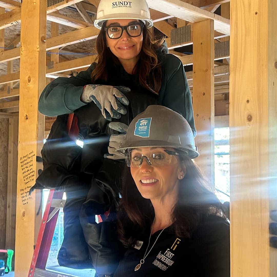 Two members of the First Impression Ironworks team. posing for a picture together, with new home framing in the background.