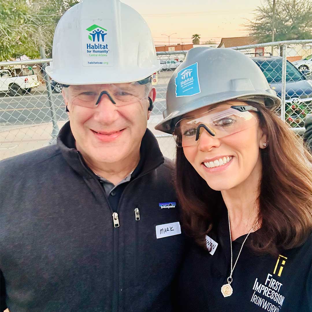 Two First Impression Ironworks employees posing for a picture while wearing hard hats 