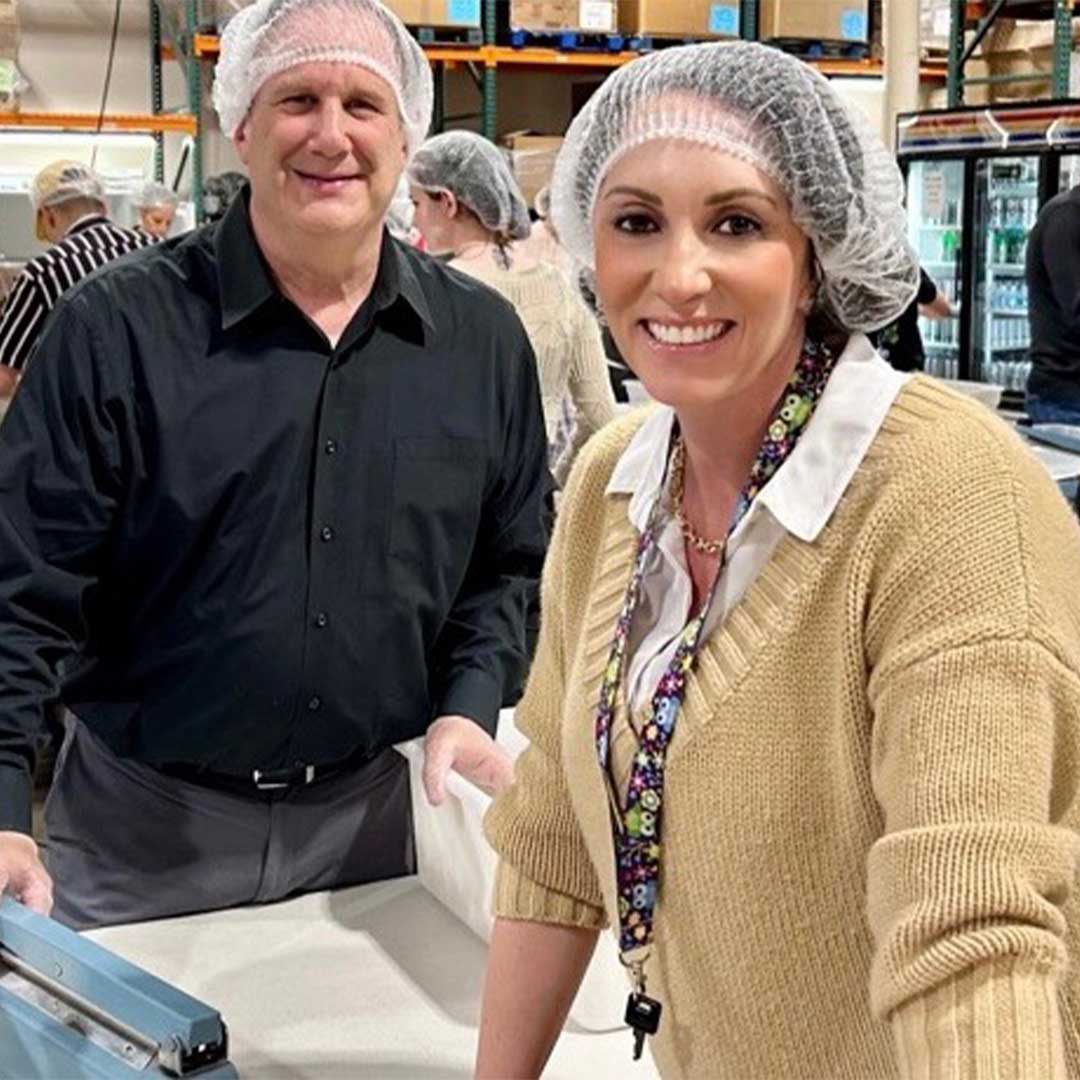 Two First Impression Ironworks employees smiling at the camera, while volunteering at Midwest Food Bank